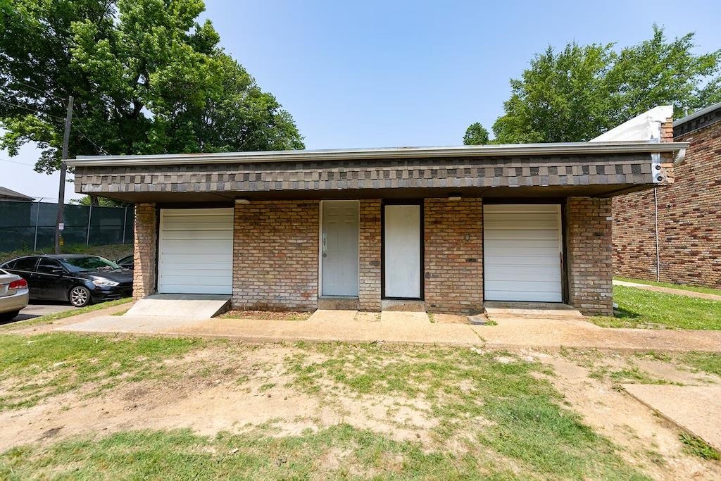 3236 Millington Road Memphis, TN 38127 - Photo 20 of 31 Brick exterior structure featuring two garage bays with white roll-up doors, a central entry door, and a covered overhang with shingle-style siding