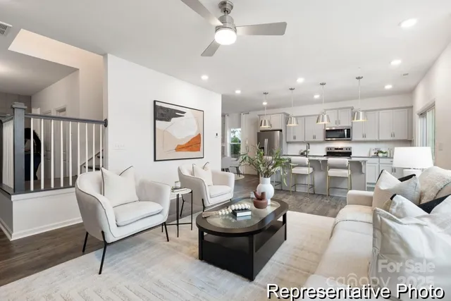 a living room with white couches and kitchen view with wooden floor