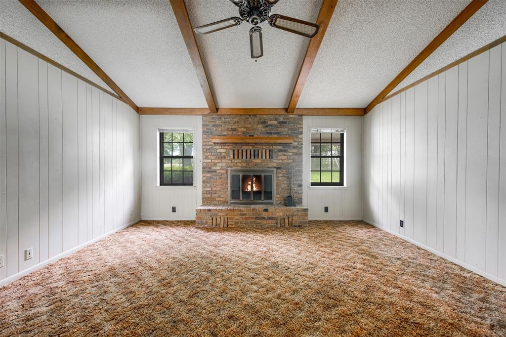8798 Hill N Dale Road Tyler, TX 75709 - Photo 9 of 31 Spacious room featuring a brick fireplace with a wood mantle, exposed wood ceiling beams, white vertical paneling, and two windows with black frames