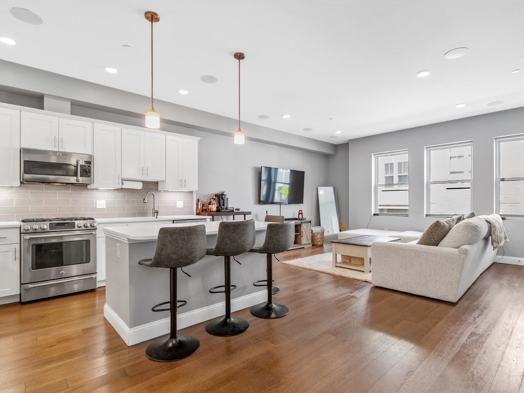 a living room with stainless steel appliances kitchen island granite countertop a stove a sink a refrigerator and white cabinets with wooden floor