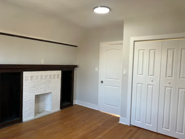 a view of an empty room with wooden floor and a fireplace