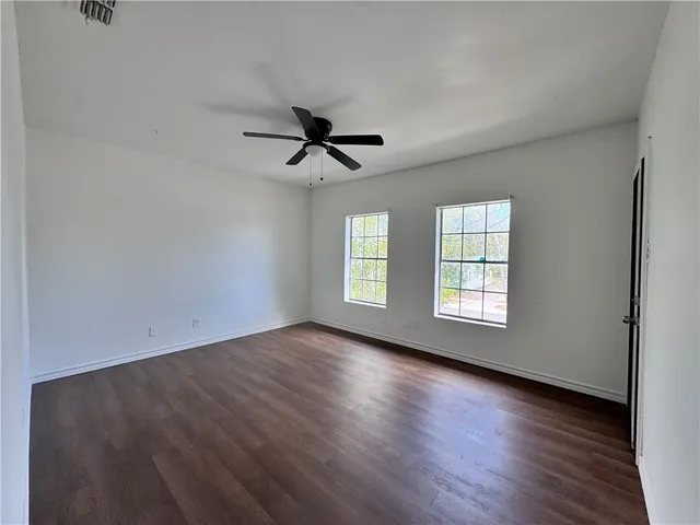 an empty room with wooden floor fan and windows