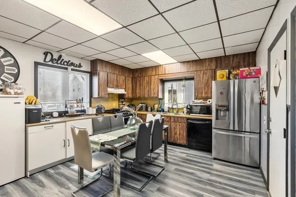 a kitchen with stainless steel appliances granite countertop a refrigerator a sink dishwasher a stove a dining table and chairs with wooden floor