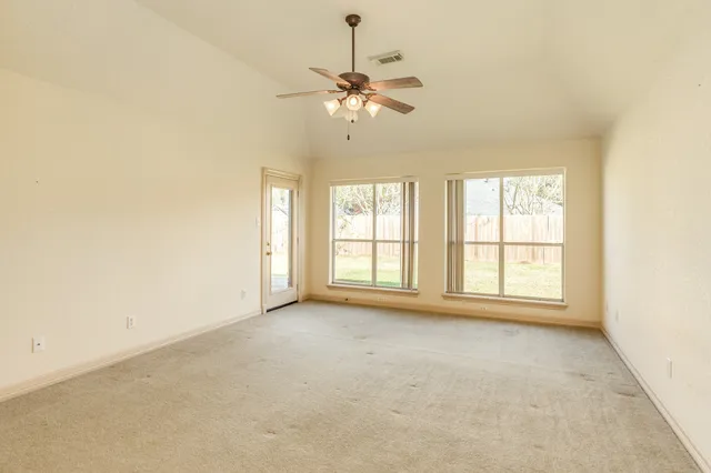 an empty room with chandelier fan and windows