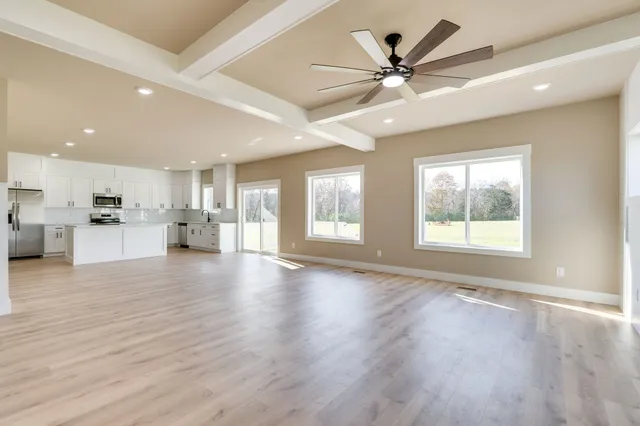 a view of an empty room with wooden floor and a kitchen