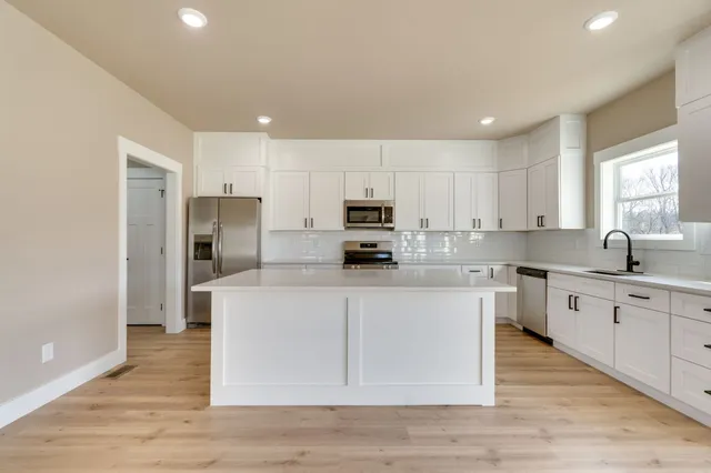 a kitchen with stainless steel appliances granite countertop a stove a sink a refrigerator and white cabinets with wooden floor