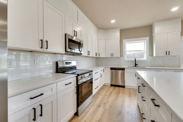 a kitchen with stainless steel appliances granite countertop wooden cabinets a sink a stove a refrigerator and white cabinets