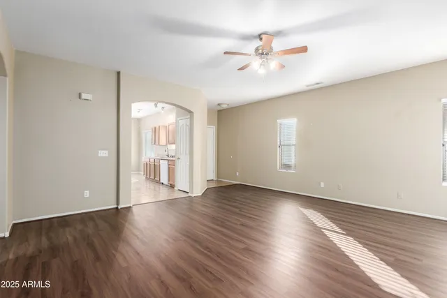 a view of an empty room with wooden floor and a ceiling fan