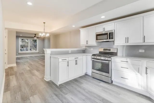 a kitchen with stainless steel appliances white cabinets a sink a stove a microwave and wooden floors