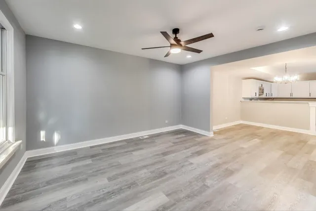 an empty room with wooden floor fan and windows