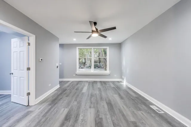 an empty room with wooden floor chandelier fan and windows