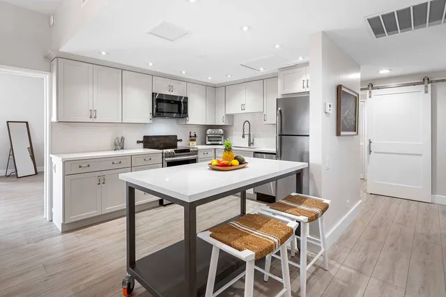 a kitchen with stainless steel appliances a dining table chairs refrigerator and sink