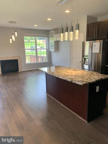 a room with stainless steel appliances kitchen island granite countertop a refrigerator a oven a sink with wooden cabinets and wooden floor