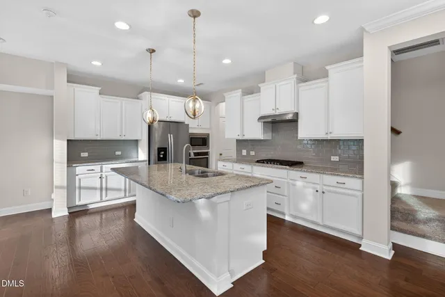 a kitchen with stainless steel appliances granite countertop a stove a sink a refrigerator and white cabinets with wooden floor