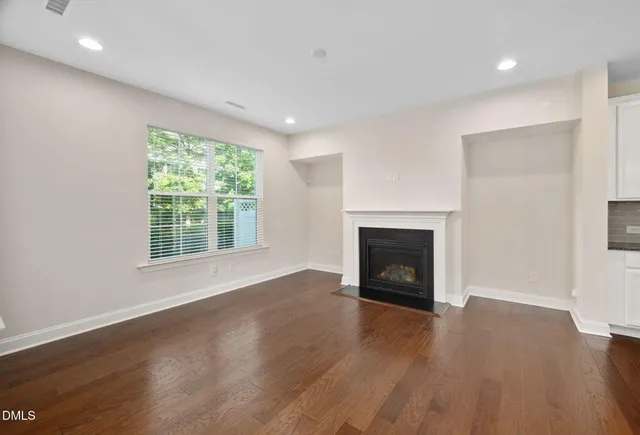 an empty room with wooden floor fire place and windows