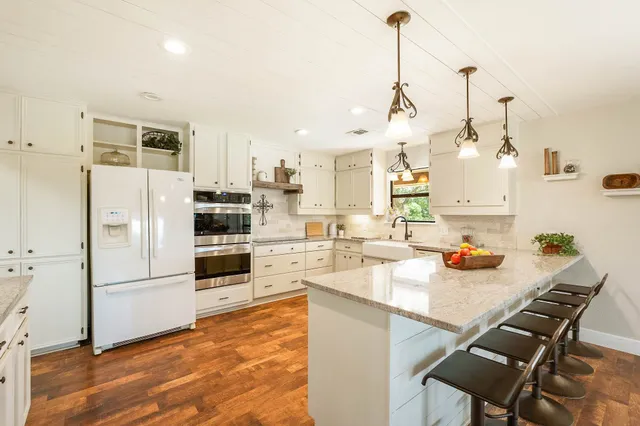 a kitchen with stainless steel appliances kitchen island granite countertop a refrigerator a sink dishwasher and white cabinets with wooden floor