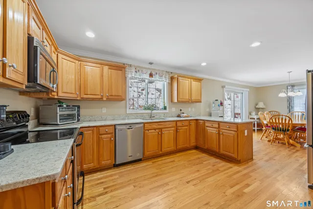 a kitchen with stainless steel appliances granite countertop wooden cabinets a sink a stove a dining table and chairs