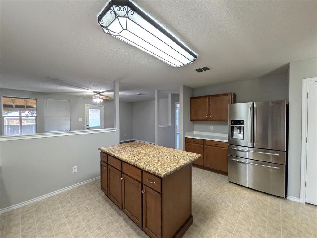 1736 Carolina Ridge Way Fort Worth, TX 76247 - Photo 13 of 33 Kitchen featuring a central island with a stone-finish countertop, wood cabinetry, and stainless steel refrigerator
