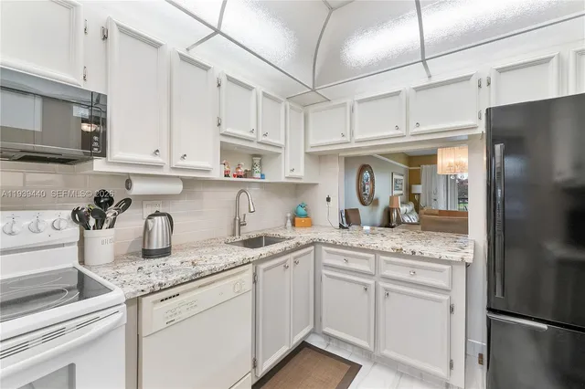 a kitchen with stainless steel appliances granite countertop a sink a refrigerator and white cabinets