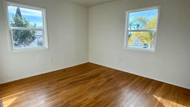 a view of an empty room with wooden floor and windows