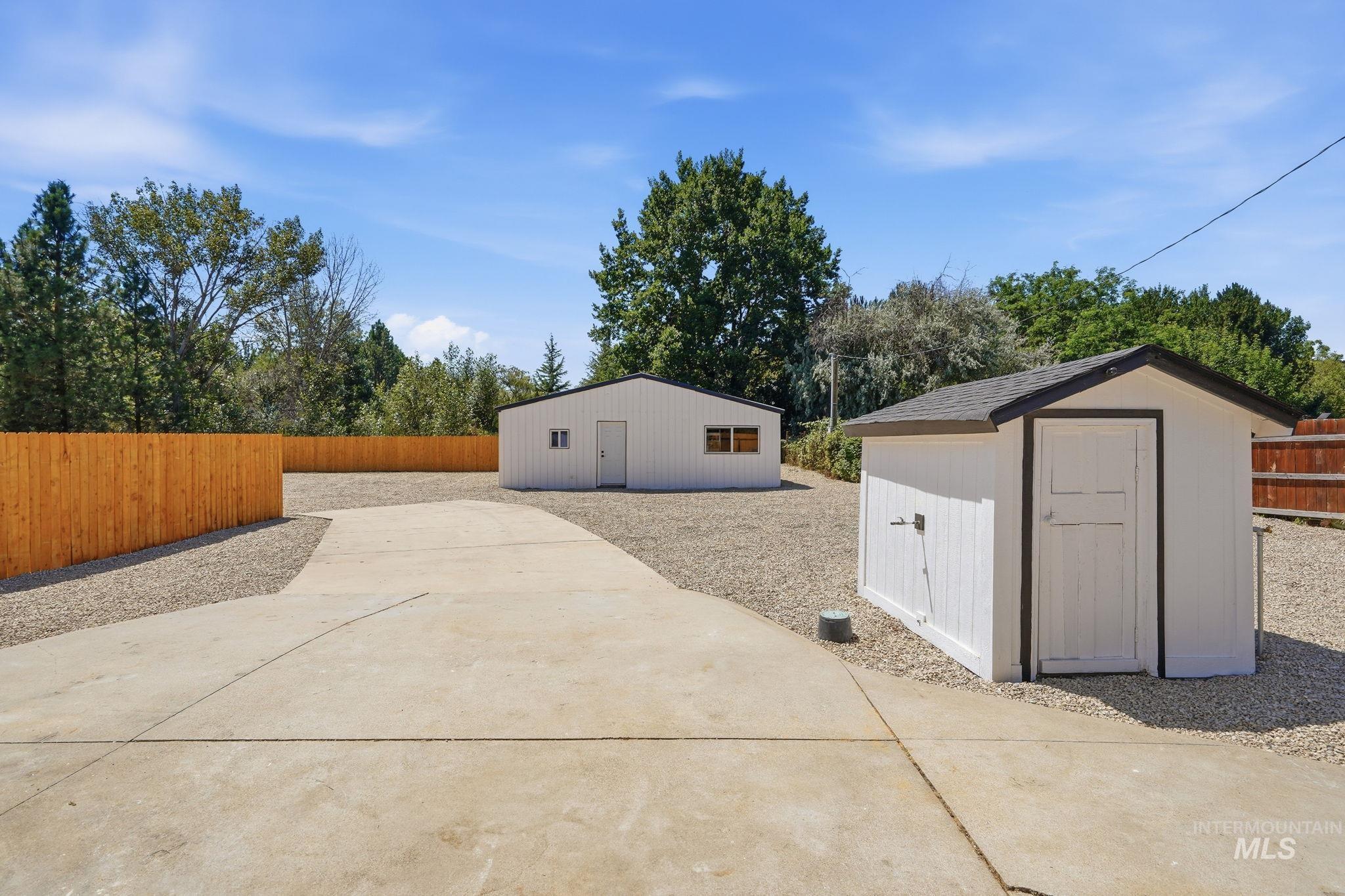 2152 Artesian Road Eagle, ID 83616 - Photo 45 of 50 Expansive gravel yard featuring a concrete driveway, a white outbuilding with a dark roof, and a separate white storage shed with a dark roof