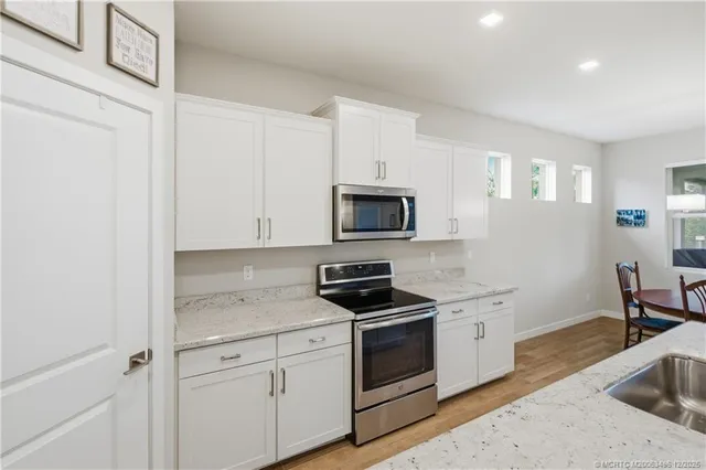a large white kitchen with a stove a sink dishwasher and a refrigerator with wooden floor