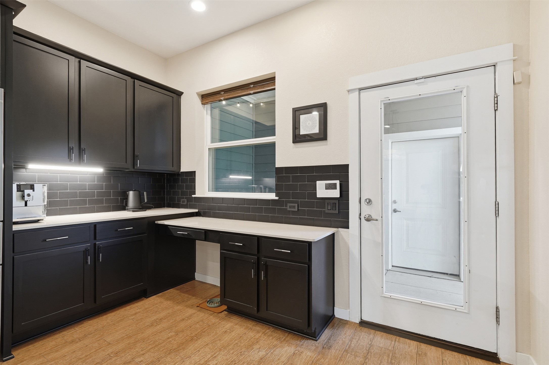 3901 Vaughan Street Austin, TX 78723 - Photo 13 of 37 Modern kitchen featuring dark cabinetry, subway tile backsplash, light-toned countertops, and wood-finish flooring