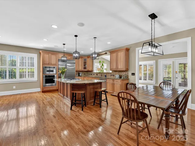 a dining room with stainless steel appliances kitchen island granite countertop a stove a refrigerator a kitchen island a dining table and chairs with wooden floor