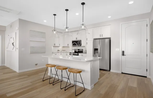 a kitchen with stainless steel appliances granite countertop a refrigerator a sink dishwasher a stove and white cabinets with wooden floor