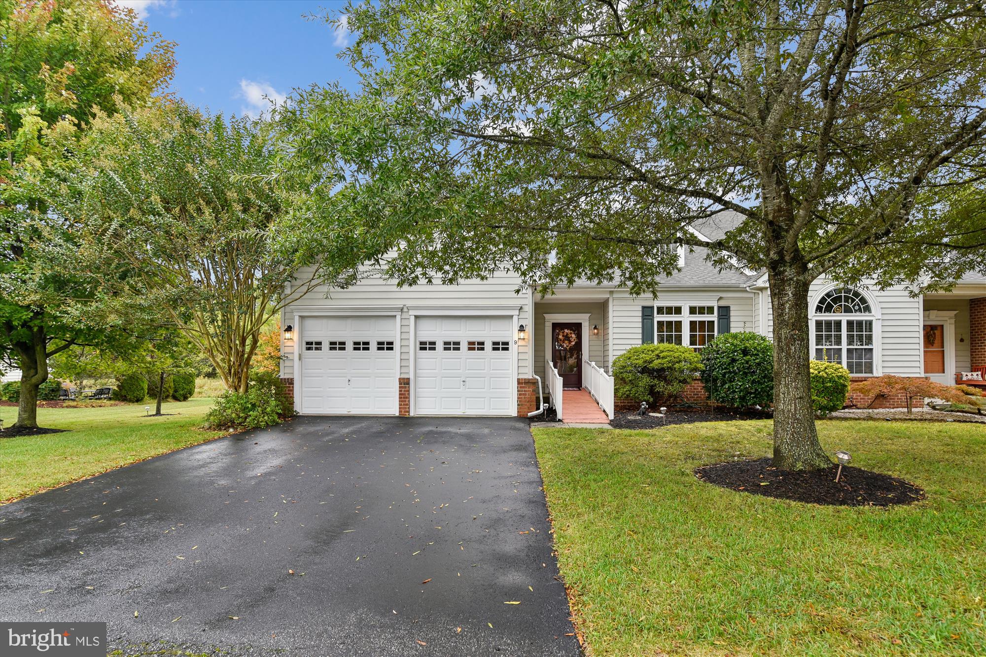 a view of a white house with a big yard and potted plants and large trees