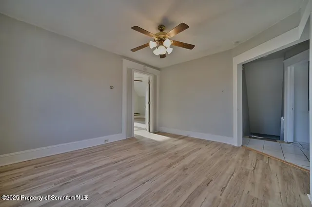 a view of an empty room with wooden floor and a ceiling fan