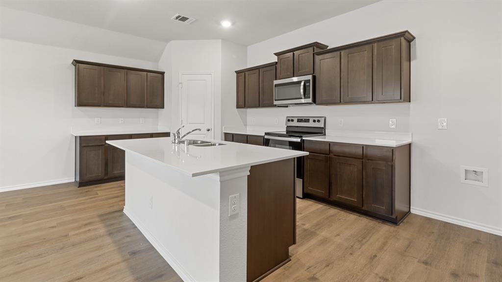 1913 Reveille Way Terrell, TX 75160 - Photo 6 of 35 Kitchen featuring stainless steel appliances, dark wood finish cabinets, an island with sink, light wood-type flooring, and light stone countertops