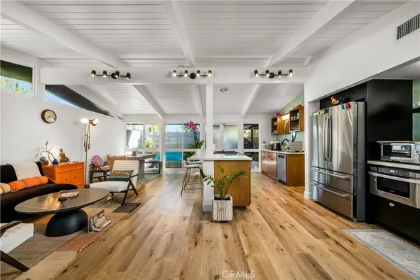 a kitchen with stainless steel appliances granite countertop a refrigerator a sink dishwasher a stove and a dining table with wooden floor