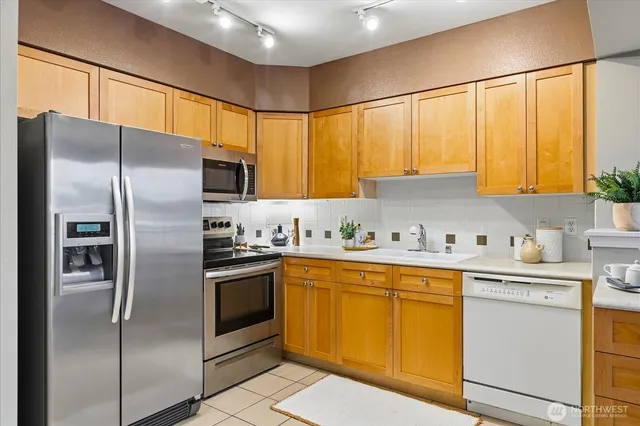 a kitchen with stainless steel appliances granite countertop a refrigerator a sink dishwasher a stove with white cabinets and wooden floor