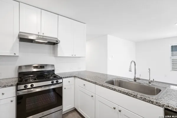 a kitchen with granite countertop a sink dishwasher a stove and cabinets