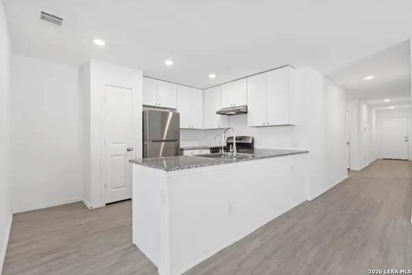 a kitchen with stainless steel appliances granite countertop a refrigerator a sink a stove a microwave and white cabinets with wooden floor