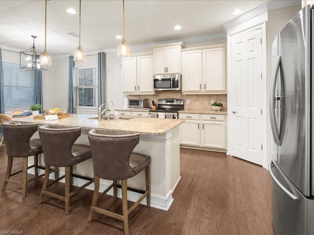 16242 Aberdeen Way Naples, FL 34110 - Photo 9 of 30 a kitchen with stainless steel appliances granite countertop a table chairs wooden floors and a view of living room