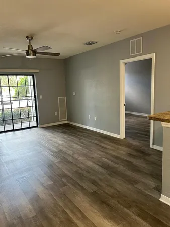 an empty room with wooden floor fan and windows