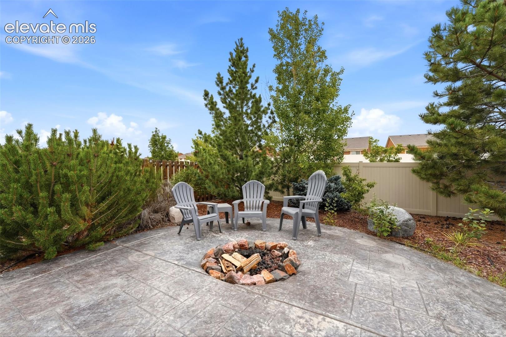 7274 Red Cardinal Loop Colorado Springs, CO 80908 - Photo 27 of 33 Stamped concrete patio featuring a built-in stone fire pit, mature trees, and privacy fencing