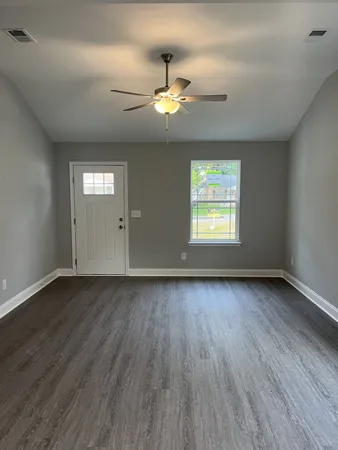 an empty room with wooden floor chandelier fan and windows