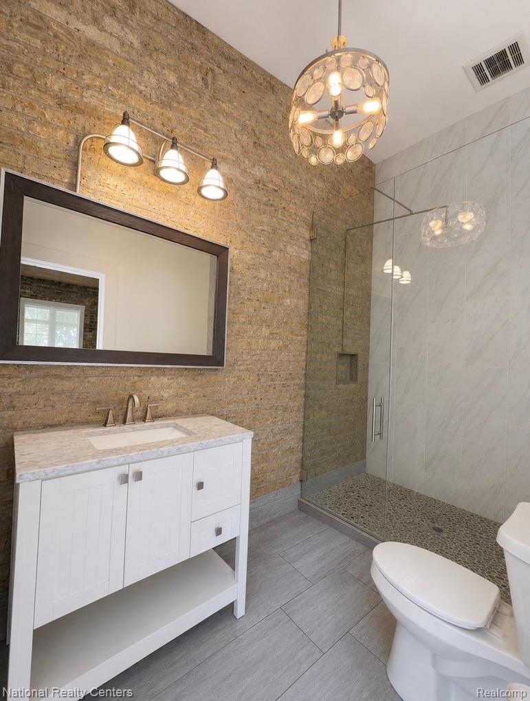 17 West Lawrence Street, Unit 2D Pontiac, MI 48342 - Photo 9 of 12 Contemporary bathroom featuring a floating vanity with an integrated sink, a glass-enclosed shower with pebble flooring, and a unique stone accent wall