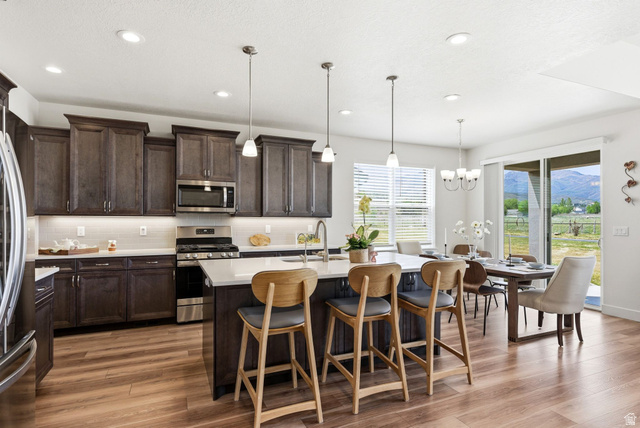 108 West Monte Rosa Lane Midway, UT 84049 - Photo 4 of 48 Open-concept kitchen with wood-finish flooring, dark wood cabinetry, white countertops, stainless steel appliances, and a central island with pendant lighting