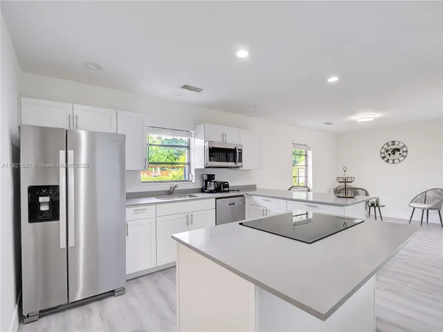 a kitchen with stainless steel appliances granite countertop a refrigerator a sink dishwasher a oven with white cabinets and wooden floor