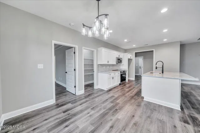 an empty room with wooden floor chandelier fan and windows