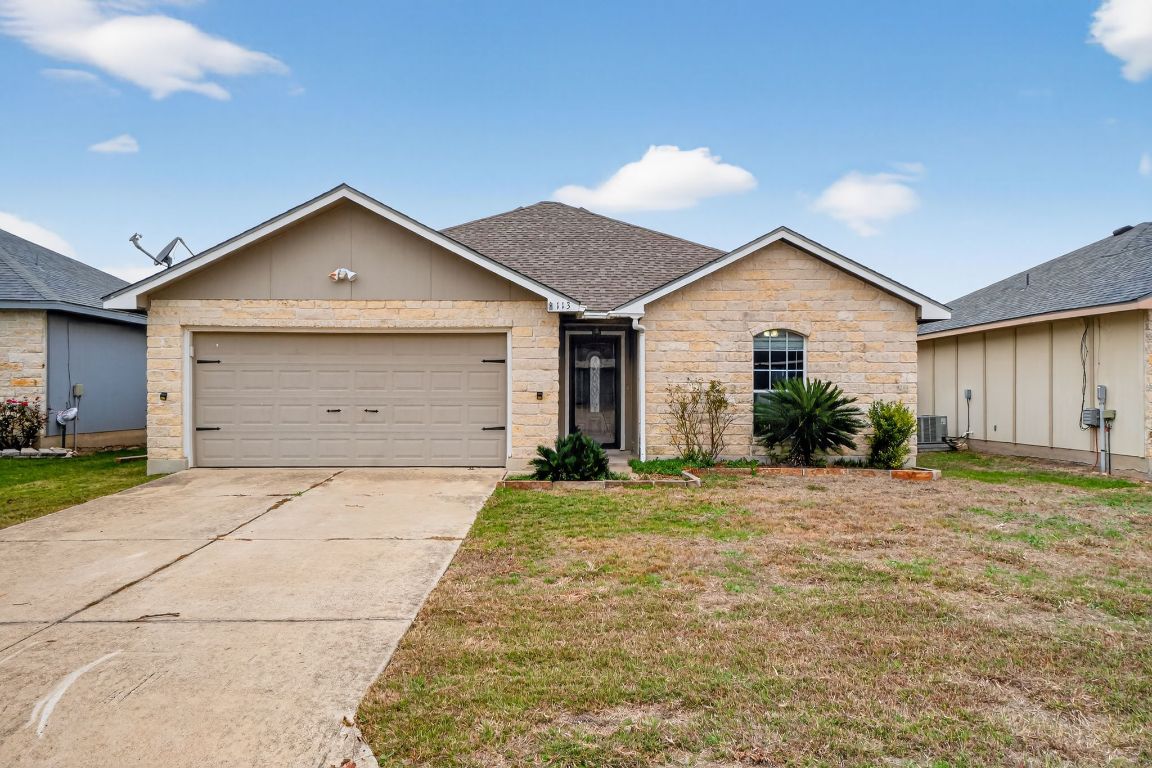 Ranch-style home with a shingled roof, a front lawn, driveway, a garage, and stone siding