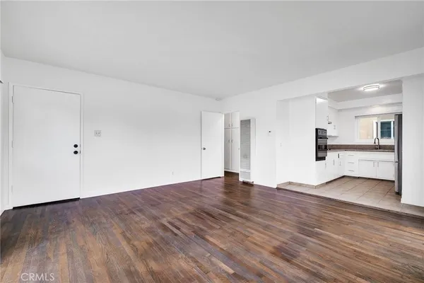 a view of an empty room with wooden floor and a kitchen
