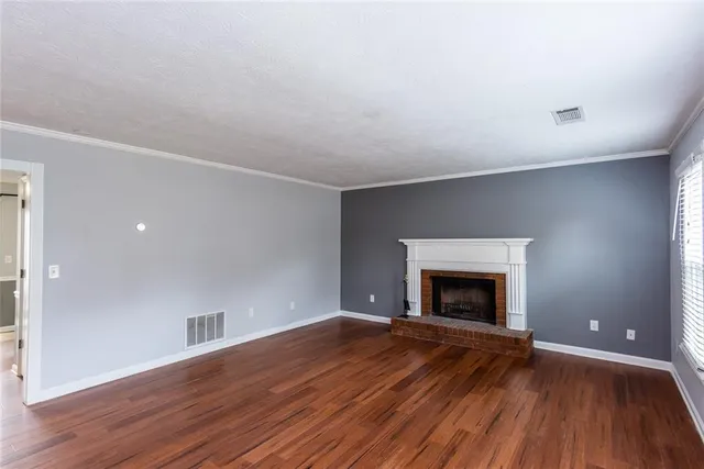 an empty room with wooden floor fireplace and windows