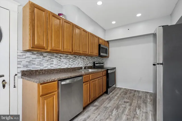 a kitchen with stainless steel appliances granite countertop a refrigerator a sink dishwasher and wooden cabinets with wooden floor