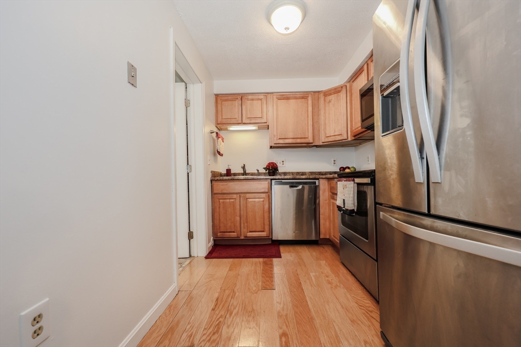 5 East Ridge Road, Unit A Merrimack, NH 03054 - Photo 13 of 19 a kitchen with stainless steel appliances granite countertop a refrigerator a sink dishwasher a stove and white countertops with wooden floor
