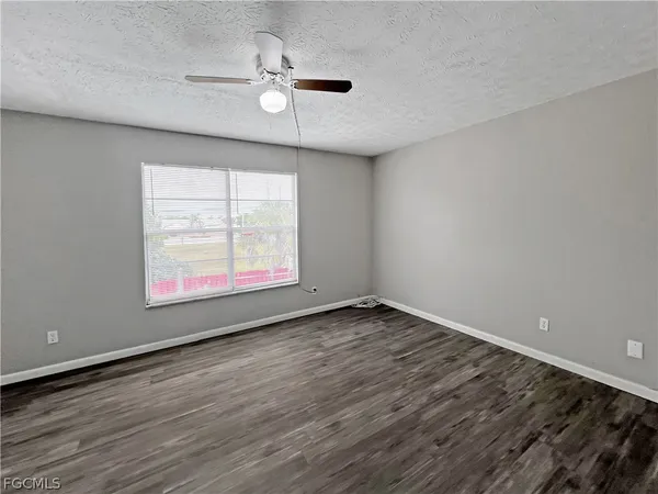 an empty room with wooden floor chandelier fan and windows